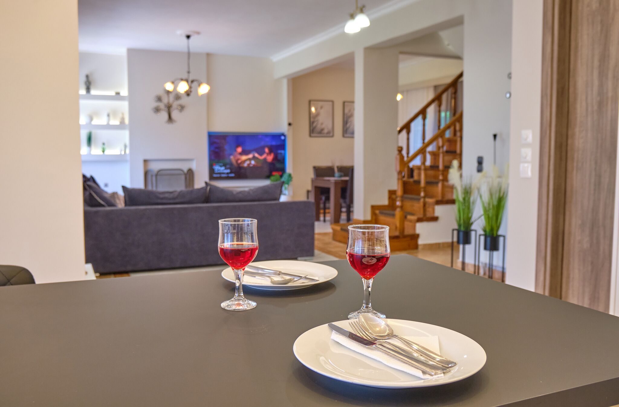 A dining table with two plates, each with a glass of red wine and cutlery.