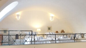Ein Schlafzimmer mit gewölbter Decke, einem Bett mit weißer Bettwäsche, einem Nachttisch, einer Lampe und zwei Wandleuchten.