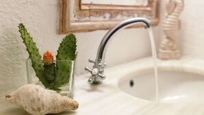 Ein Waschbecken mit einer Glasvase, in der ein Kaktus und eine Muschel liegen.