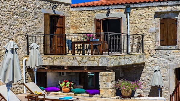 A stone building with a balcony, outdoor seating, and potted plants.