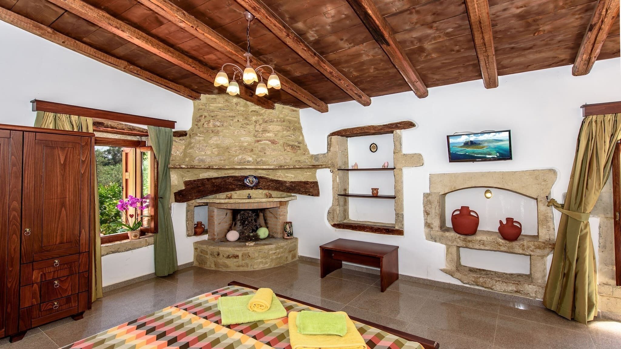 A rustic room with a stone fireplace, wooden beams, a wooden cabinet, and a bed with a colorful quilt.