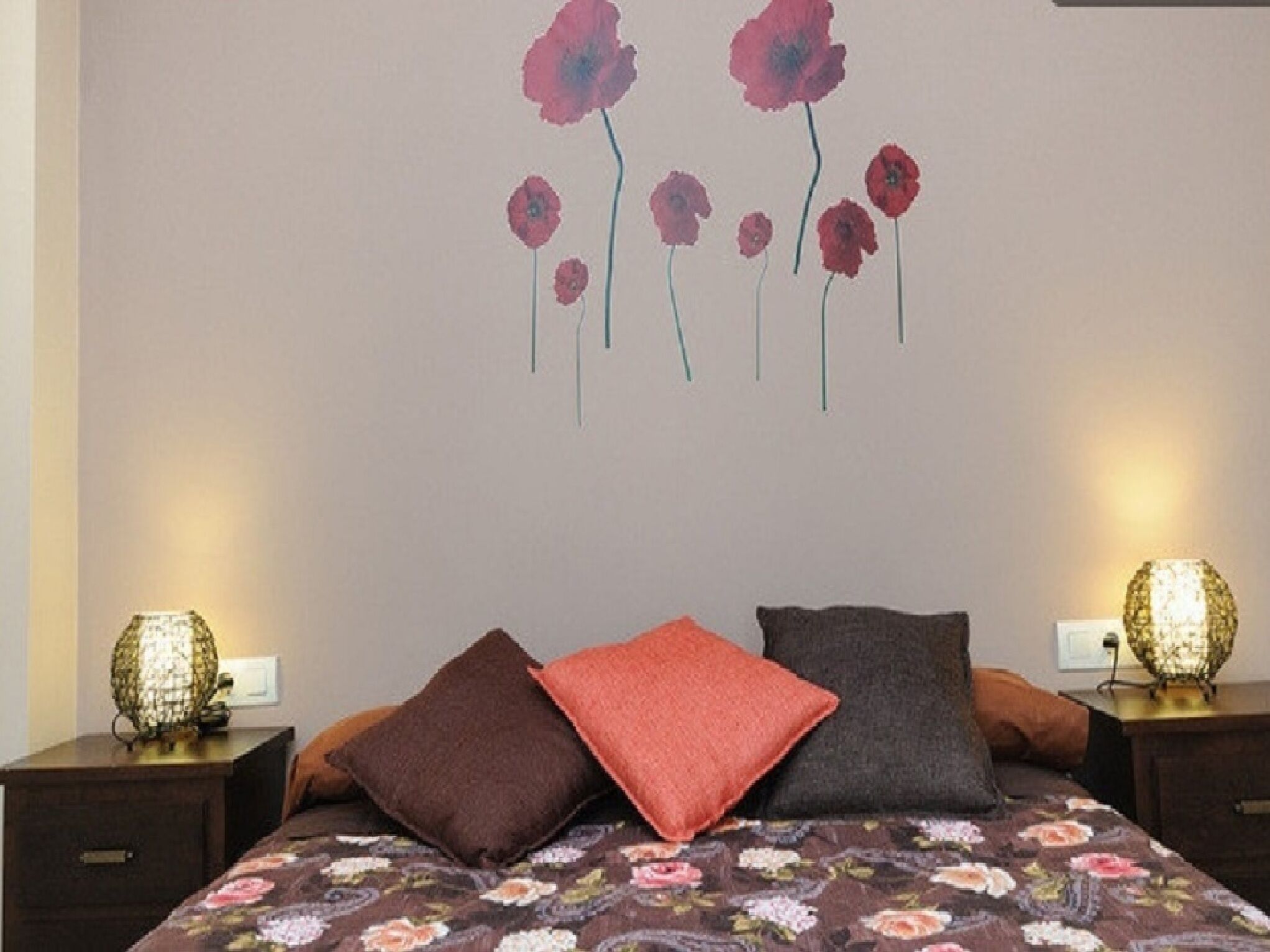 A bedroom with a floral bedspread, two bedside lamps, and a wall mural of flowers.
