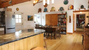 A kitchen with a wooden island, a dining area with chairs and a table, and a bookshelf filled with books. - 18th Century Mill House in a Courtyard Setting (.)