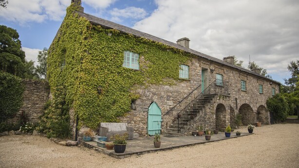 A stone building with ivy-covered walls, a wooden door, and a staircase leading to an upper level. - 18th Century Mill House in a Courtyard Setting (.)