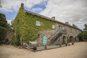 A stone building with ivy-covered walls, a wooden door, and a staircase leading to an upper level.