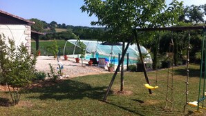 Ein Garten mit Gewächshaus, Schaukel und Pool.