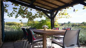 Eine Terrasse im Freien mit einem Holztisch und Stühlen, umgeben von Grünpflanzen und Blick auf die Landschaft.