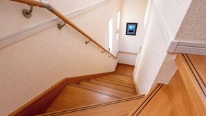 Una escalera de madera con barandilla, un cuadro en la pared y una puerta al final.