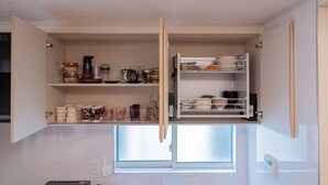 Una cocina compacta con alacenas abiertas, un ventanal y una encimera con diversos utensilios de cocina.