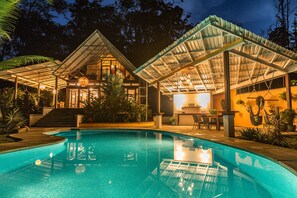 Una piscina con una veranda coperta, circondata da vegetazione rigogliosa e un ambiente interno ben illuminato.