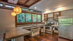 Una cocina con piso de madera, un ventanal con vista a follaje, horno empotrado y refrigerador de acero inoxidable.