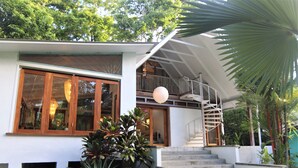 Una casa moderna con una escalera que lleva a un balcón, rodeada de vegetación.