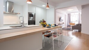Een moderne keuken met een centraal eiland, roestvrijstalen apparatuur en hangende lampen.