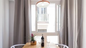 Een eettafel met een fles wijn en twee glazen, een potplant en een uitzicht op een balkon door een raam.