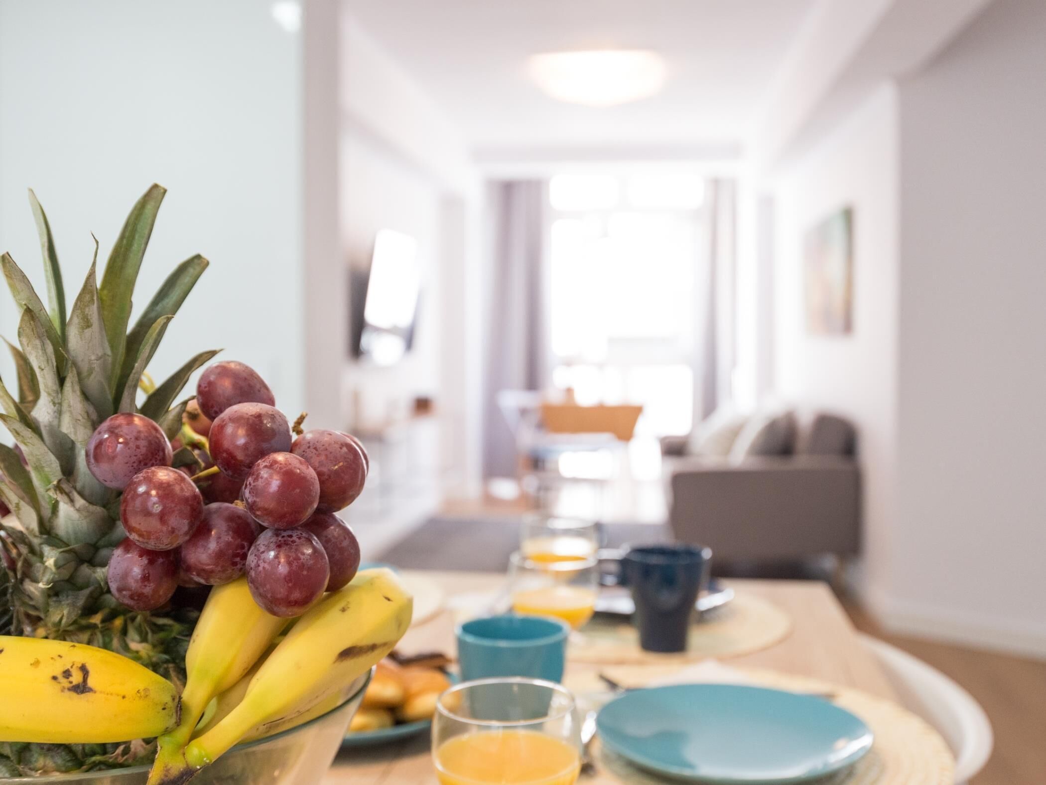 Ein Frühstückstisch mit Ananas, Bananen, Trauben und einem Glas Orangensaft.