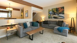 A modern living room with two grey sofas, a wooden coffee table, and a painting of a waterfall on the wall. - 2BR Courtside at Topnotch Spa (Stowe)