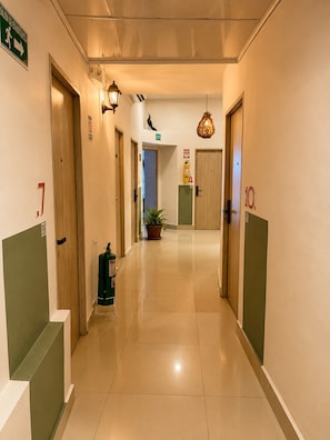 Un couloir d’hôtel avec des portes numérotées de 7 à 10, un extincteur vert et une plante en pot.