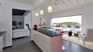 Une cuisine moderne dotée d’un îlot central en verre, de meubles blancs et offrant une vue sur l’extérieur.