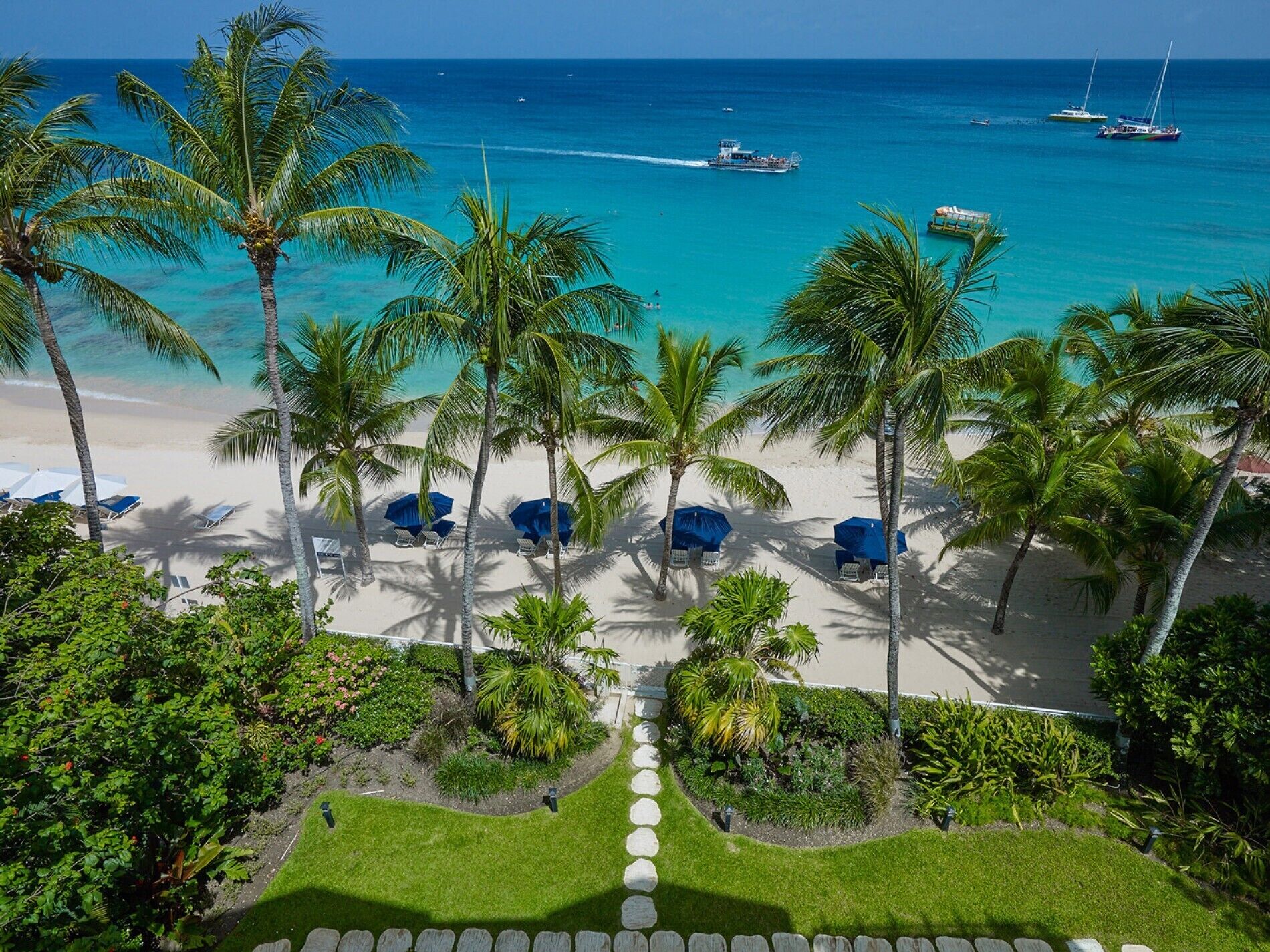 A beach view with palm trees, a clear blue sea, and boats.