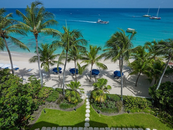 Une vue sur la plage, avec des palmiers, une mer bleue et limpide, et des bateaux.