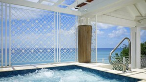 Un jacuzzi con vista al océano, rodeado por un pabellón blanco con detalles de celosía.