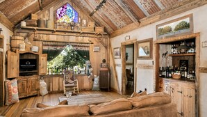 Un interior rústico con techo de madera, un ventanal de vitral, una zona de bar con botellas y un área de descanso acogedor.