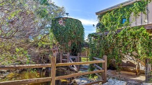 Un jardín rústico con un puente de madera, una fuente de piedra y un edificio parcialmente cubierto de hiedra.