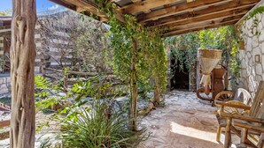 Un patio rústico al aire libre con vigas de madera, muros de piedra y diversas plantas.