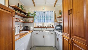 Una cocina compacta con armarios blancos, repisas de madera y una ventana con cortinas azules.
