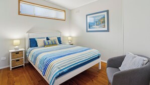 Un dormitorio con cama, mesitas de noche, una silla, una ventana y un cuadro en la pared.