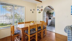 Un comedor con una mesa y sillas de madera, un cuenco de fruta y vista al patio trasero a través de una ventana.