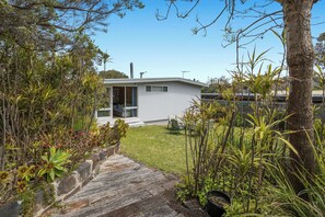 Ein modernes Haus mit überdachter Terrasse, umgeben von üppiger Vegetation und einem Kiesweg, der zum Eingang führt.