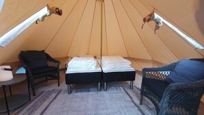 A cozy tent with two beds, wicker chairs, a small table, and a hanging light fixture.