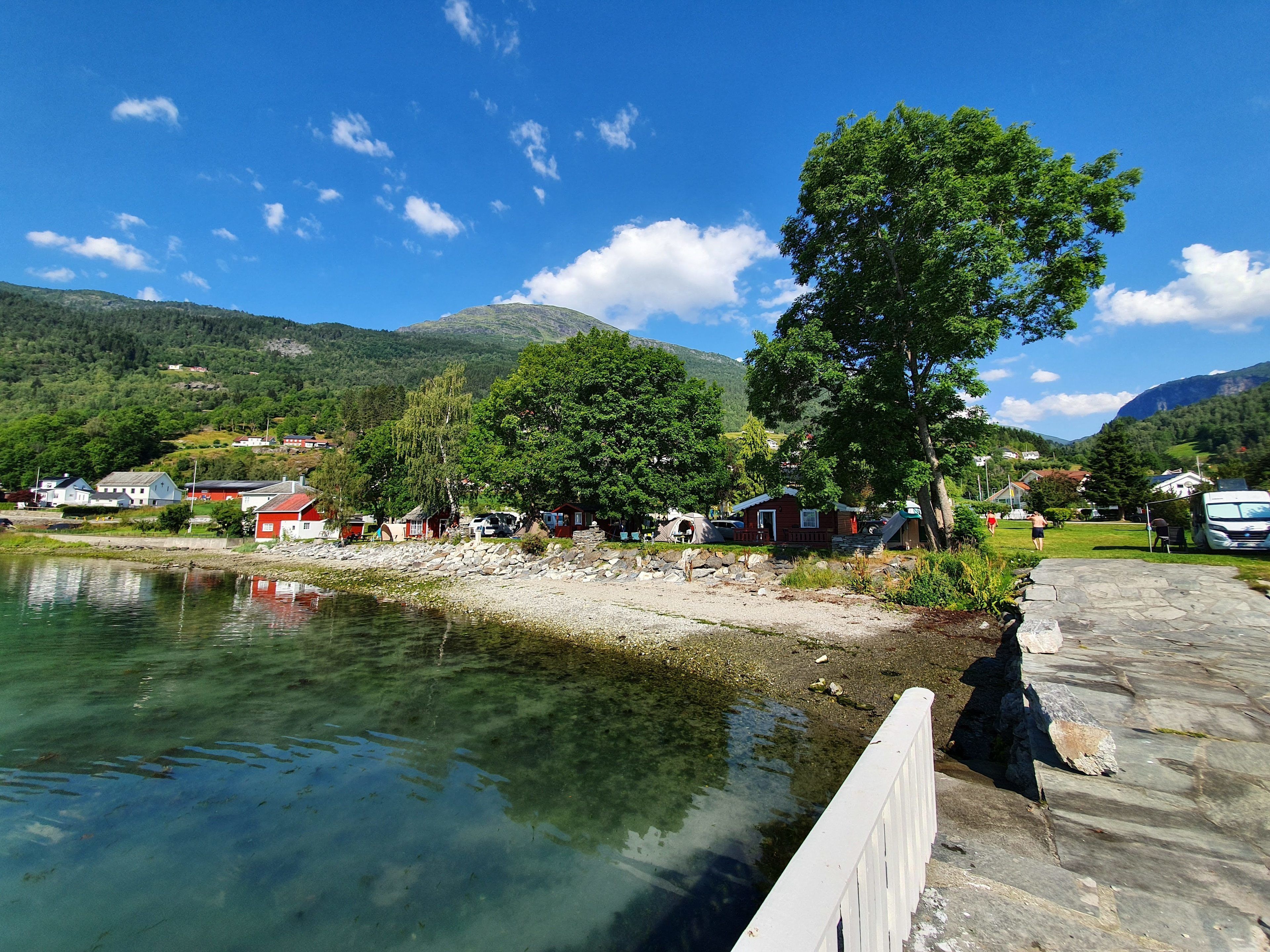 A lakeside cabin with a dock, surrounded by trees and a mountain backdrop.