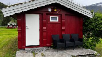 A red wooden cabin with a white door, numbered 14, and three wicker chairs outside.