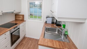 A compact kitchen with white cabinets, a wooden countertop, a built-in oven, a sink with a strainer, and a window overlooking a lake.