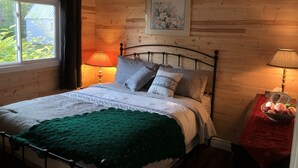 A bedroom with a wooden wall, a bed with a green blanket, two bedside lamps, and a framed picture on the wall.