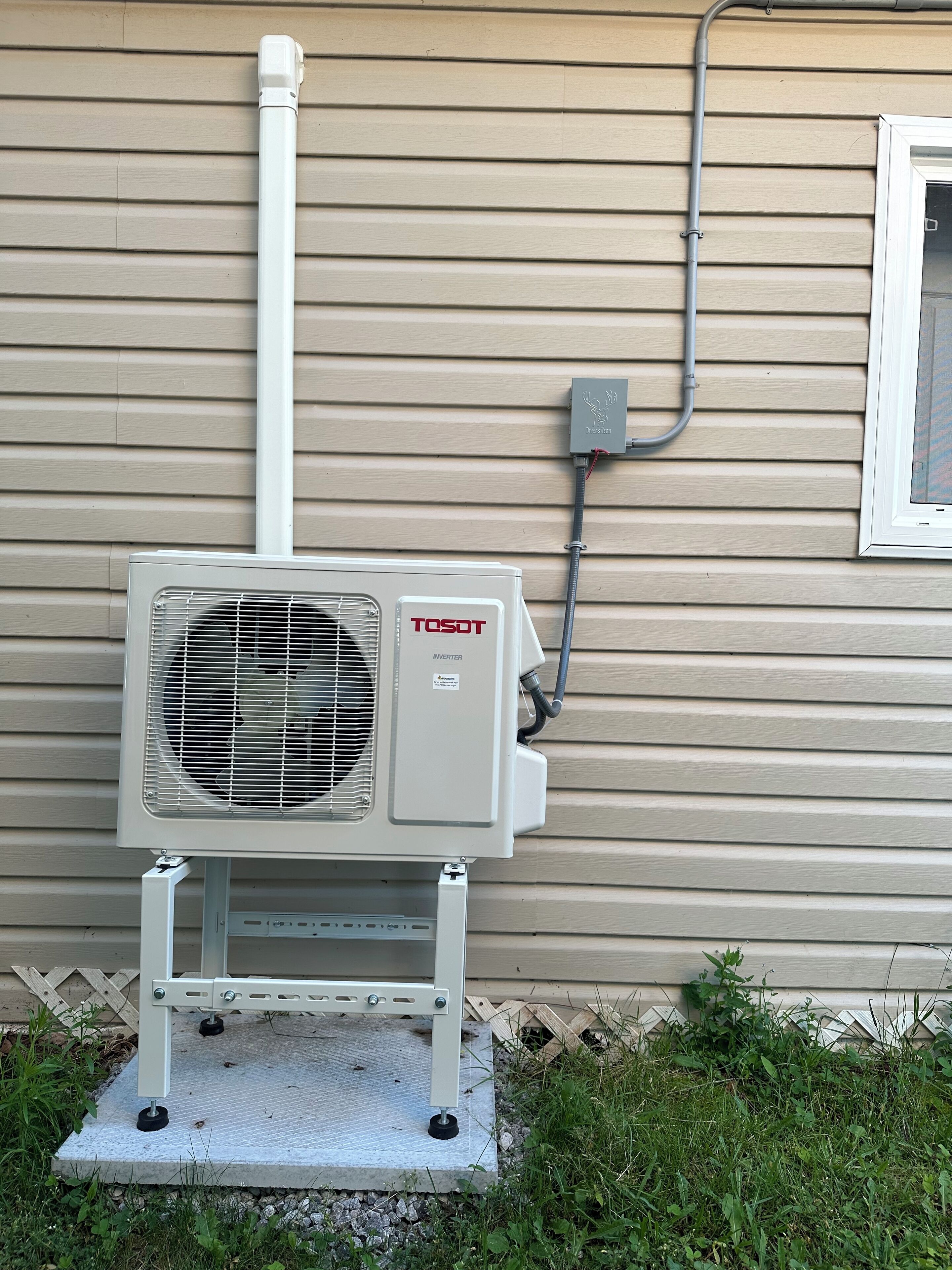 An outdoor air conditioning unit mounted on a concrete base against a beige house siding.