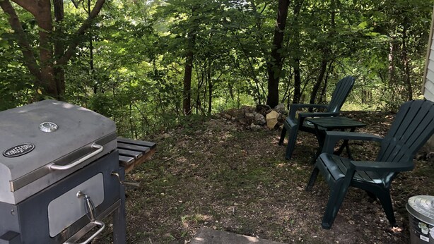 En grill och en utomhusplats med sittmöbler, belägen i en skogliknande miljö.