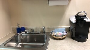 Ett kök med en diskho i rostfritt stål, en kaffemaskin från Keurig och en korg som innehåller diverse föremål.