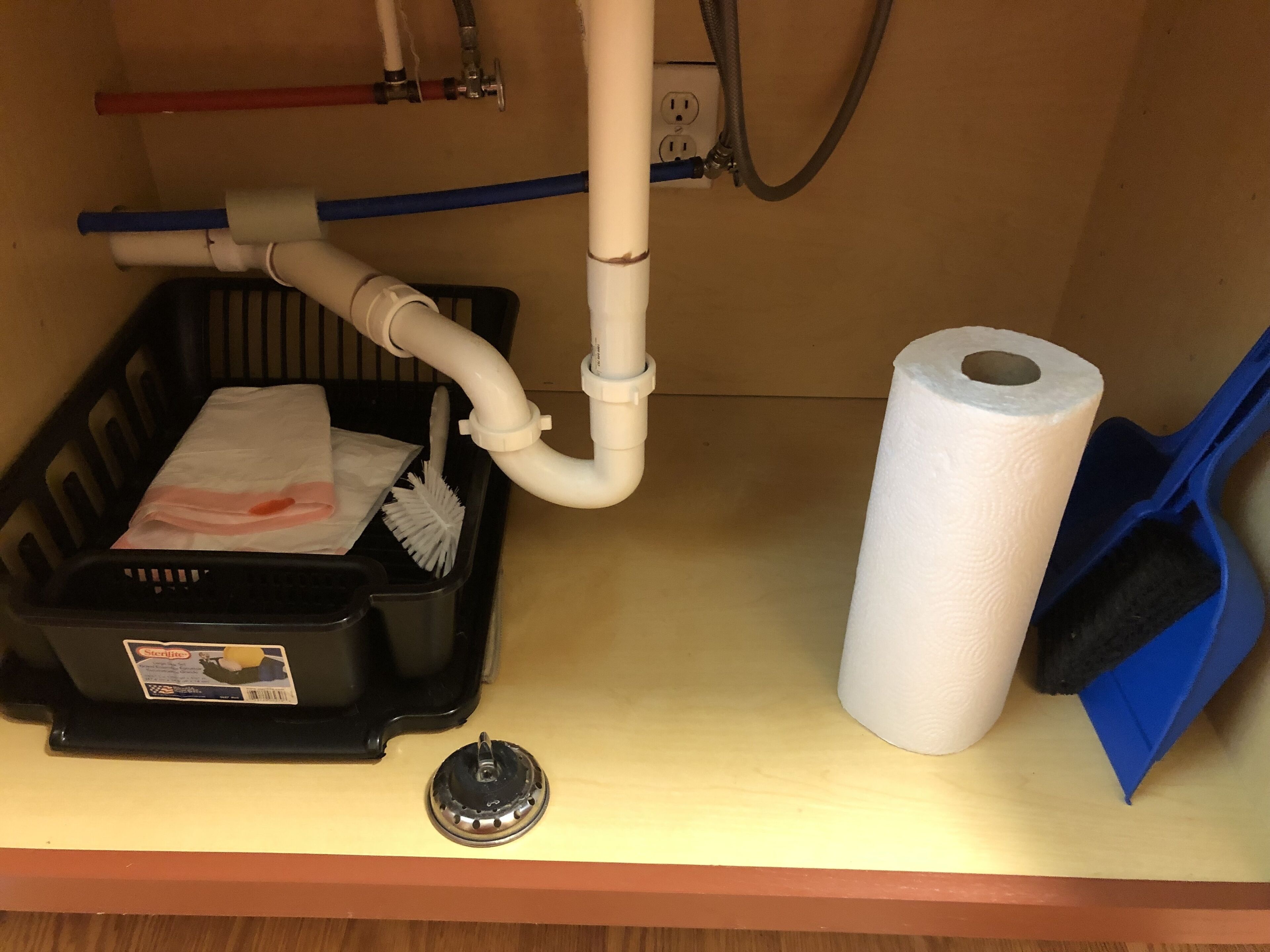 Un lavabo de salle de bain avec une poubelle noire, un rouleau de papier toilette et une brosse de nettoyage bleue.
