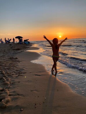 A beach scene with a child walking towards the sunset, people in the background, and beach umbrellas. - SARDINIA - CASTELSARDO - brand new apartment - CODE IUN P8066 (Lu Bagnu)
