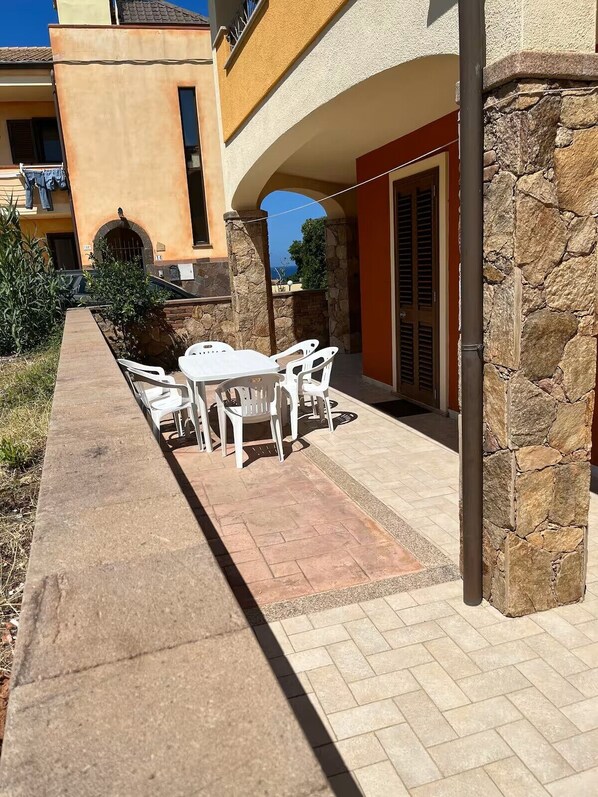 A patio with a table and chairs, a stone wall, and a view of the sea.