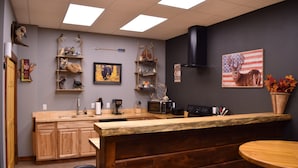 A kitchen with wooden cabinets, a microwave, and a sink. There are shelves with various items and a painting of a deer. - GREEN HILL LODGE @ thegreenhilllodge.com (Fordland)
