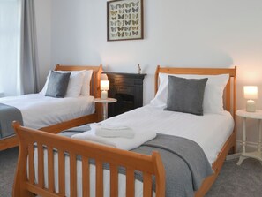 Habitación de hotel con dos camas individuales, cada una con cabecero de madera, ropa de cama blanca y una manta gris. Hay una mesita entre las camas con una lámpara, y una obra de arte con mariposas enmarcada en la pared.