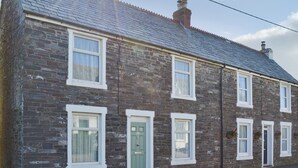A two-story stone building with a slate roof, multiple windows with white frames, and a green door. - 4 bedroom accommodation in Delabole, near Tintagel (Delabole, near Tintagel)
