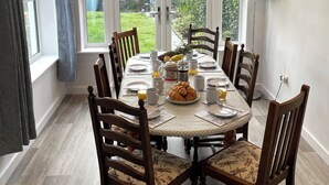 A dining table set for breakfast with chairs, a view of the garden through large windows, and a lamp on the right. - 4 bedroom accommodation in Delabole, near Tintagel (Delabole, near Tintagel)