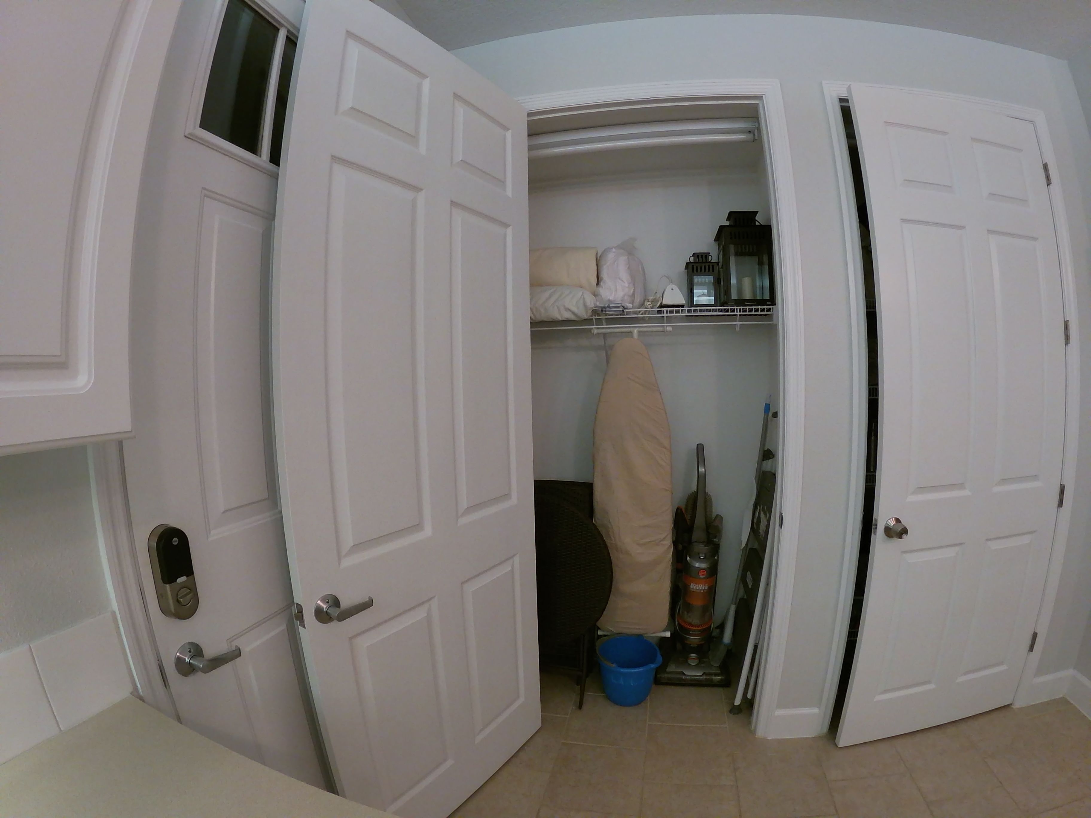 A room with white doors, a visible closet with shelves, a blue bucket, and a vacuum cleaner.