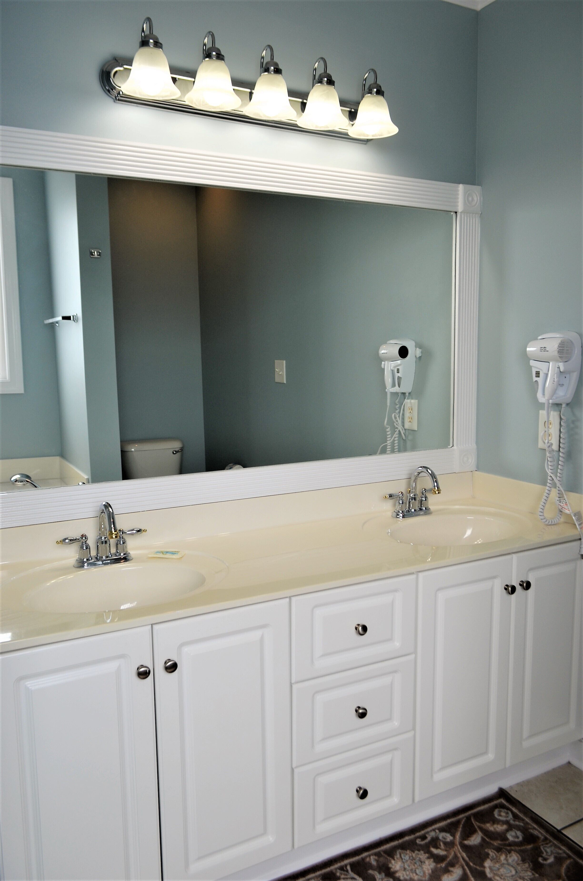 A bathroom with a double sink, a large mirror, and a hairdryer on the wall.