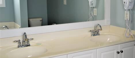 A bathroom with a double sink, a large mirror, and a hairdryer on the wall.